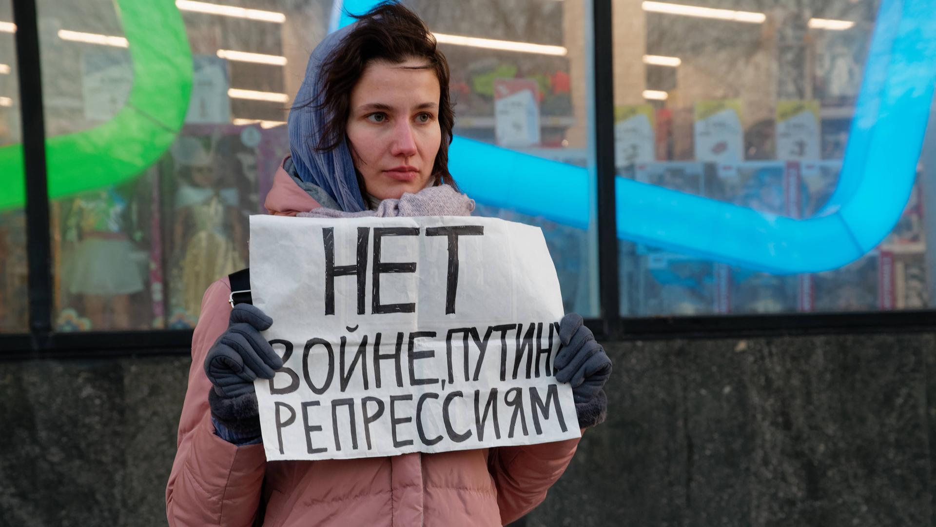 Eine Demonstrantin protestiert mit einem selbst gemalten Schild in Moskau gegen den Krieg in der Ukraine. Die junge Frau mit rosa Mantel hält das Papier vor sich. Eine Demonstrantin protestiert mit einem selbst gemalten Schild in Moskau gegen den Krieg in der Ukraine. Die junge Frau mit rosa Mantel hält das Papier vor sich.