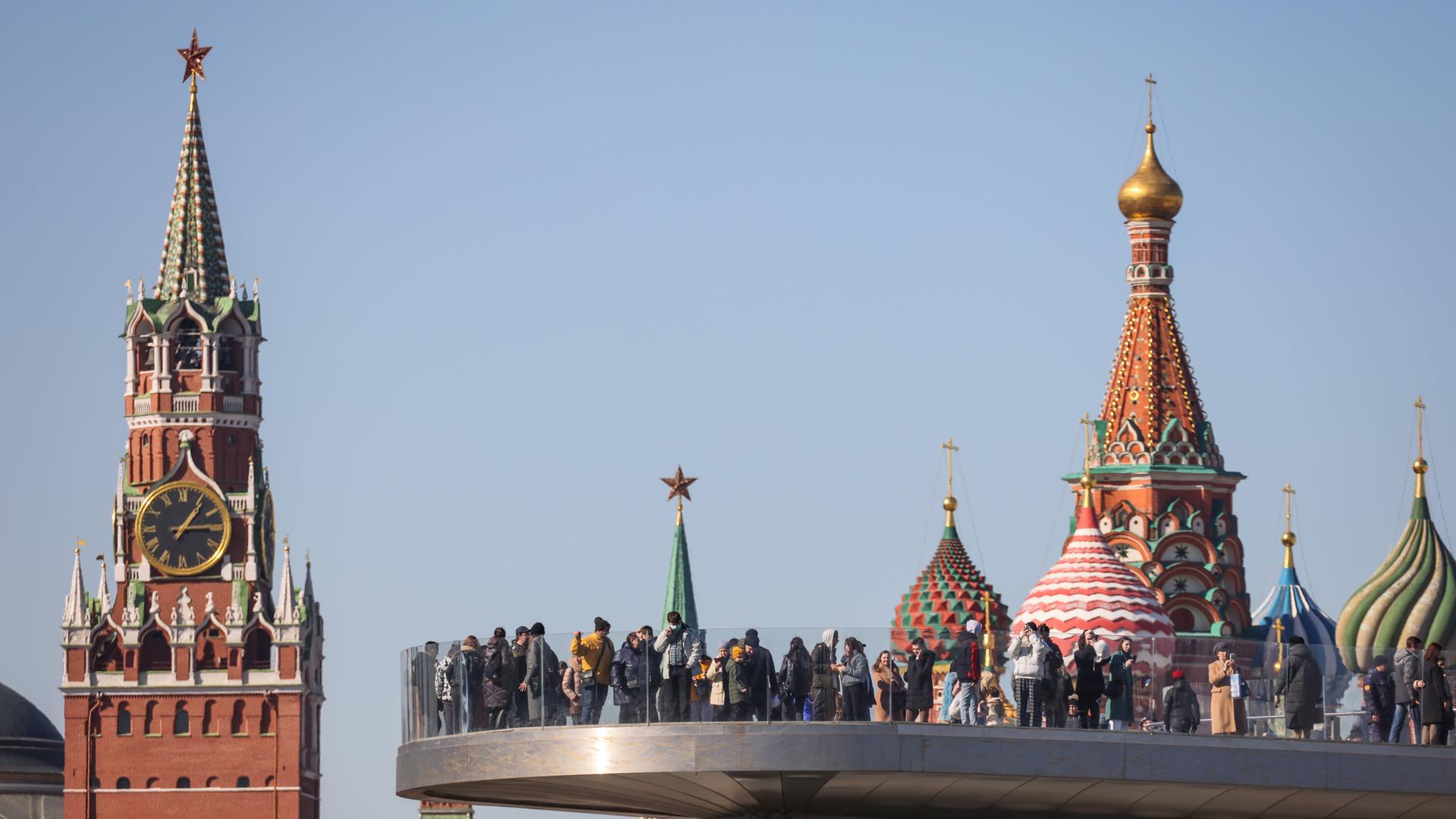 Ein Blick auf den Spasskaya-Turm des Moskauer Kremls, eine Aussichtsplattform im Zaryadye-Park und die Kuppeln der Basilius-Kathedrale Ein Blick auf den Spasskaya-Turm des Moskauer Kremls, eine Aussichtsplattform im Zaryadye-Park und die Kuppeln der Basilius-Kathedrale