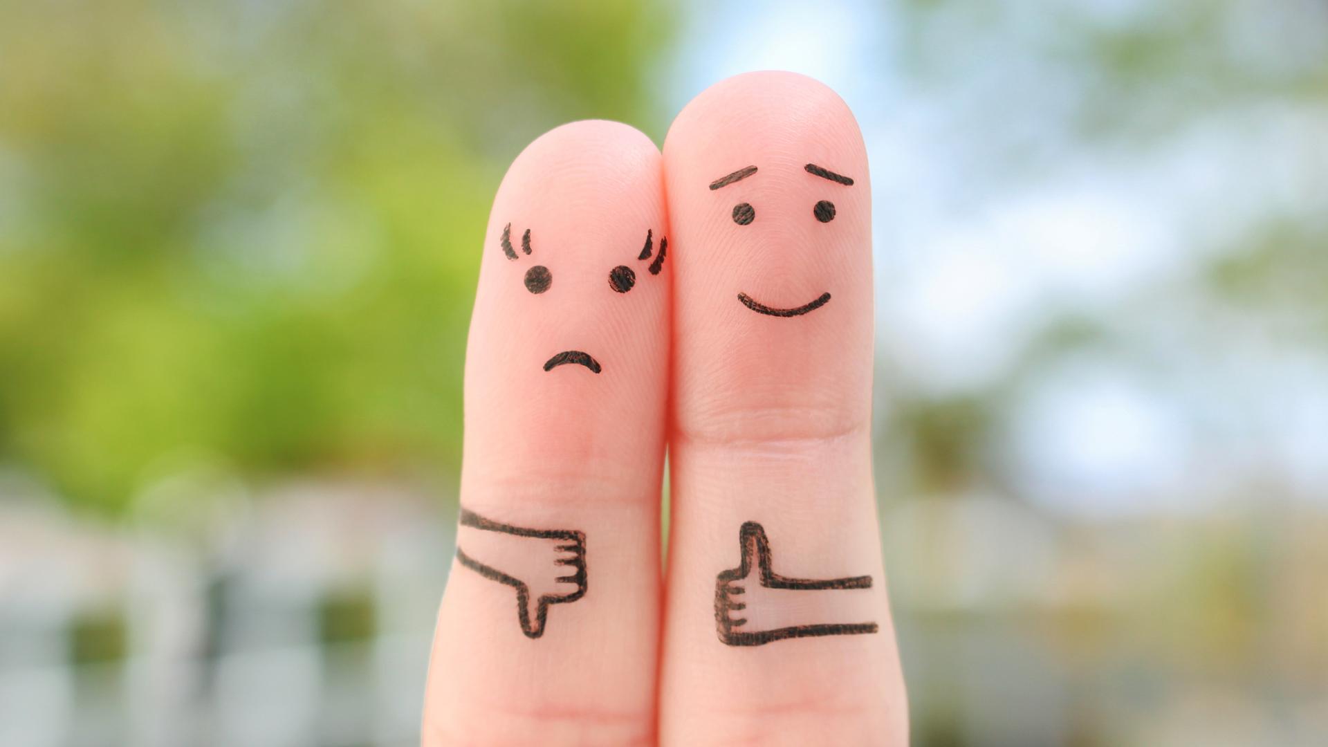 Zwei Finger, die als Figuren angemalt sind. Einer zeigt einen aufgemalten Daumen nach oben, der andere nach unten. Zwei Finger, die als Figuren angemalt sind. Einer zeigt einen aufgemalten Daumen nach oben, der andere nach unten.