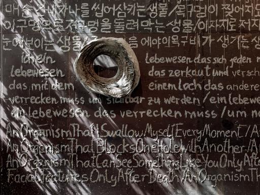 Blick in die Ausstellung im MMK: Ein auf die Wand mit einem in Flüssigbeton getauchten Zeigefinger geschriebenes Gedicht auf Deutsch, Englisch und Koreanisch.
