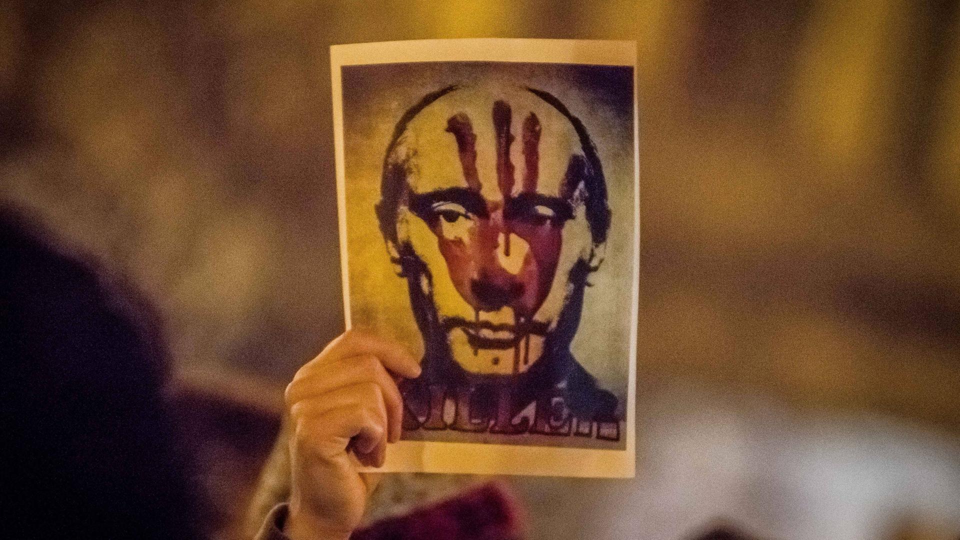 Eine Hand hält auf einer Demonstration ein Bild von Russlands Präsident Wladimir Putin hoch. Es trägt den roten Abdruck einer Hand. Eine Hand hält auf einer Demonstration ein Bild von Russlands Präsident Wladimir Putin hoch. Es trägt den roten Abdruck einer Hand.