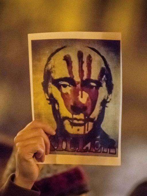 Eine Hand hält auf einer Demonstration ein Bild von Russlands Präsident Wladimir Putin hoch. Es trägt den roten Abdruck einer Hand.