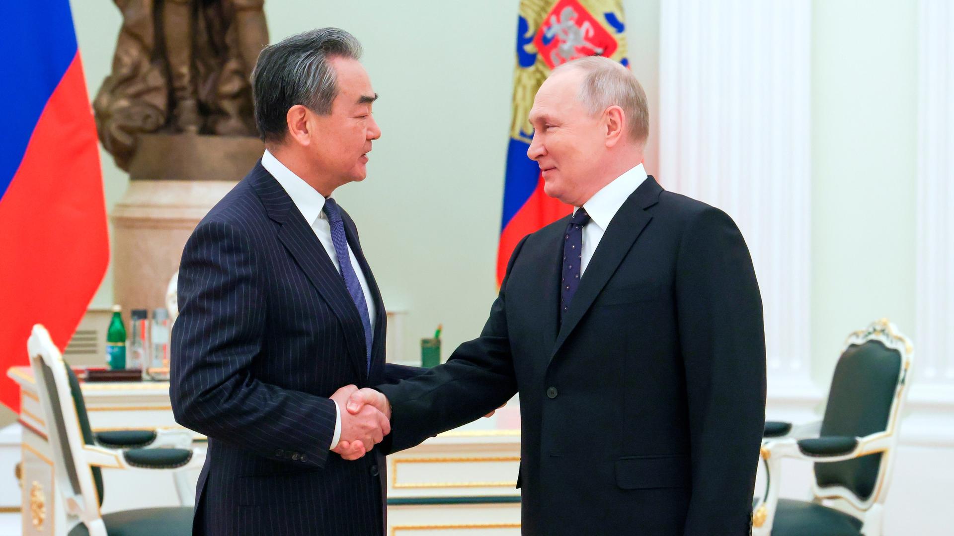 Der russische Präsident Wladimir Putin und Chinas oberster Außenpolitiker Wang Yi schütteln sich die Hände. Sie befinden sich im Kreml.