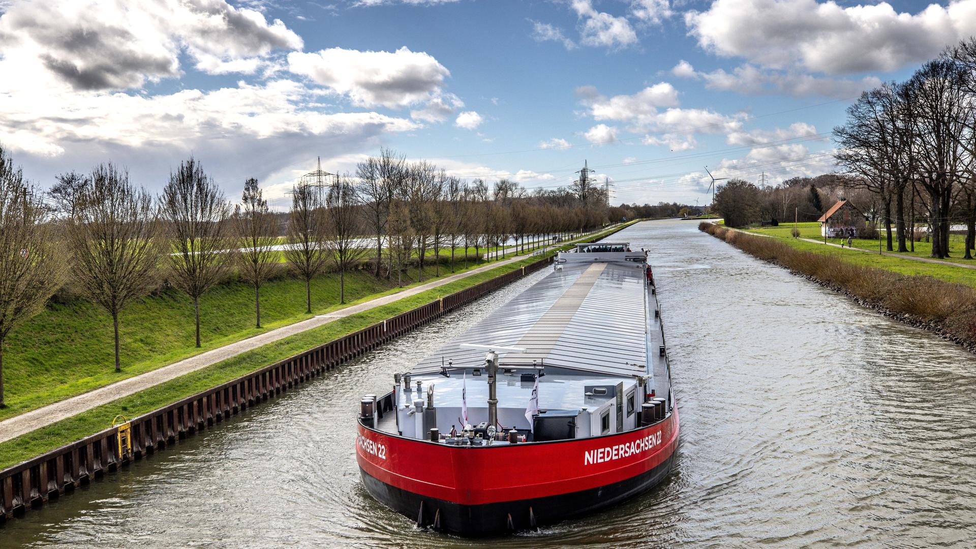 Das Schiff fährt durch den Dortmund-Ems-Kanal. Es trägt den Namen "Niedersachsen 22" in weißer Schrift auf dem rot lackierten Schiff.