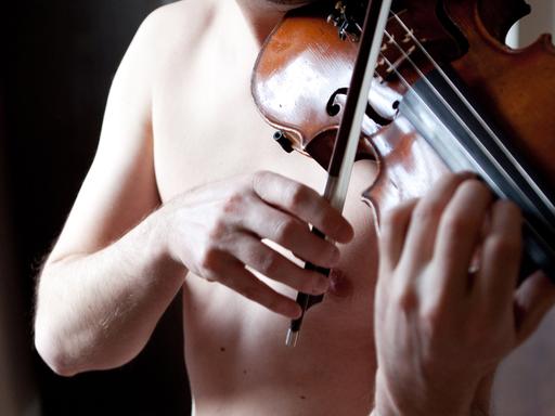 Ein junger Mann mit nacktem Oberkörper spielt auf einer Geige.