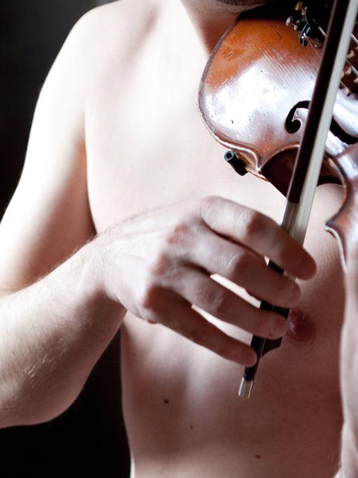 Ein junger Mann mit nacktem Oberkörper spielt auf einer Geige.