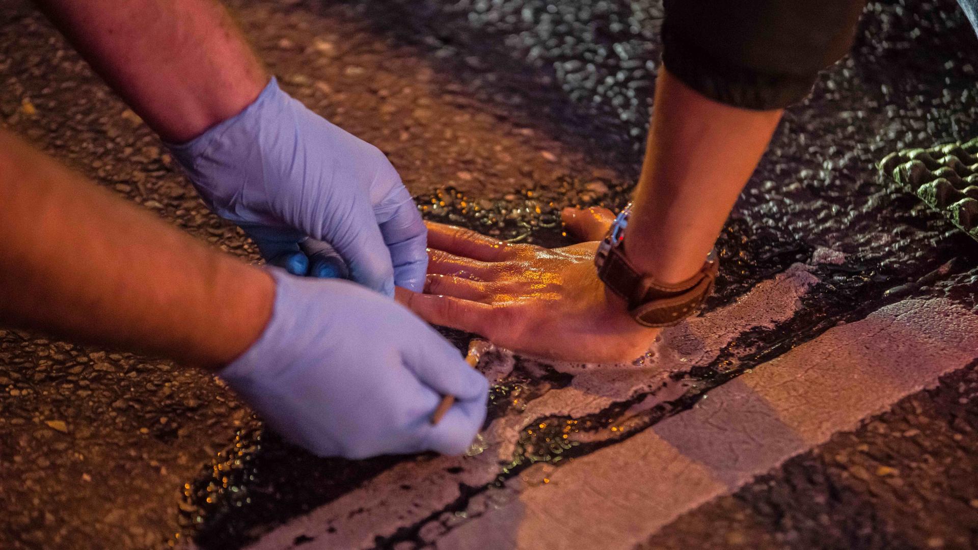 Protest der "Letzten Generation" am 7. November 2022 in München: Ein junger Mensch hat seine Hand auf der Fahrbahn festgeklebt, eine Person mit Gummihandschuhen versucht, die Klebeverbindung zu lösen.