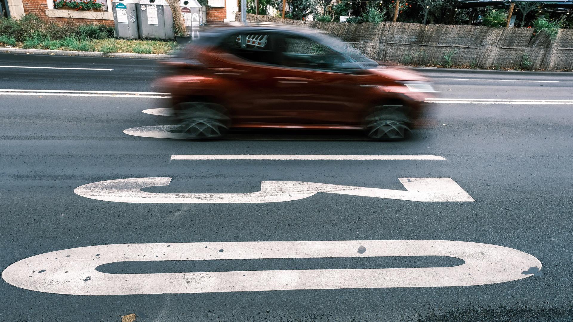 Auf einer Strasse in Düsseldorf ist vor einem fahrenden orangfarbenen Auto eine weisse "30" zu sehen.