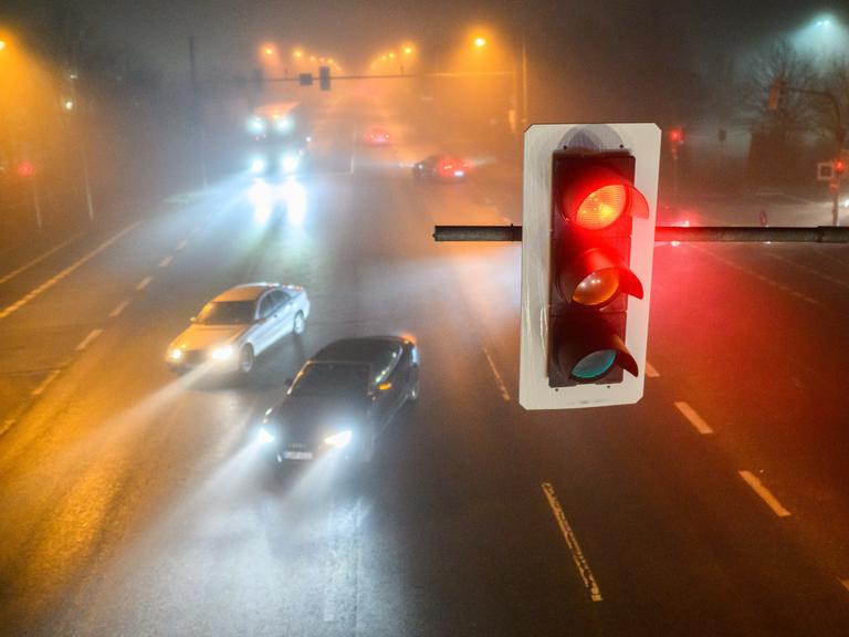 Autos passieren am frühen Morgen bei dichtem Nebel eine Kreuzung mit einer Ampel, die rot ist.