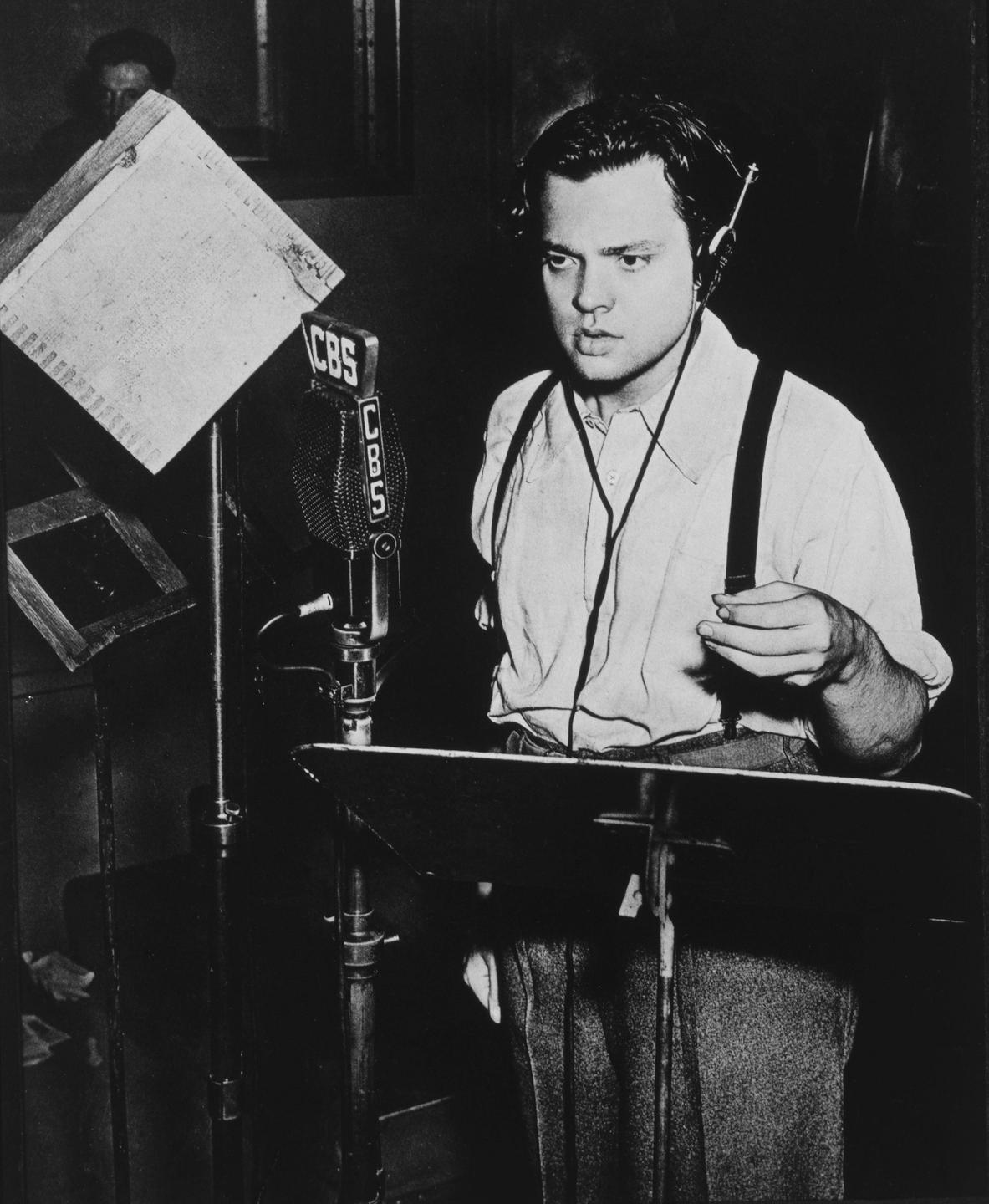Der junge Orson Welles steht in einem Studio und spricht in ein Mikrofon der CBS.