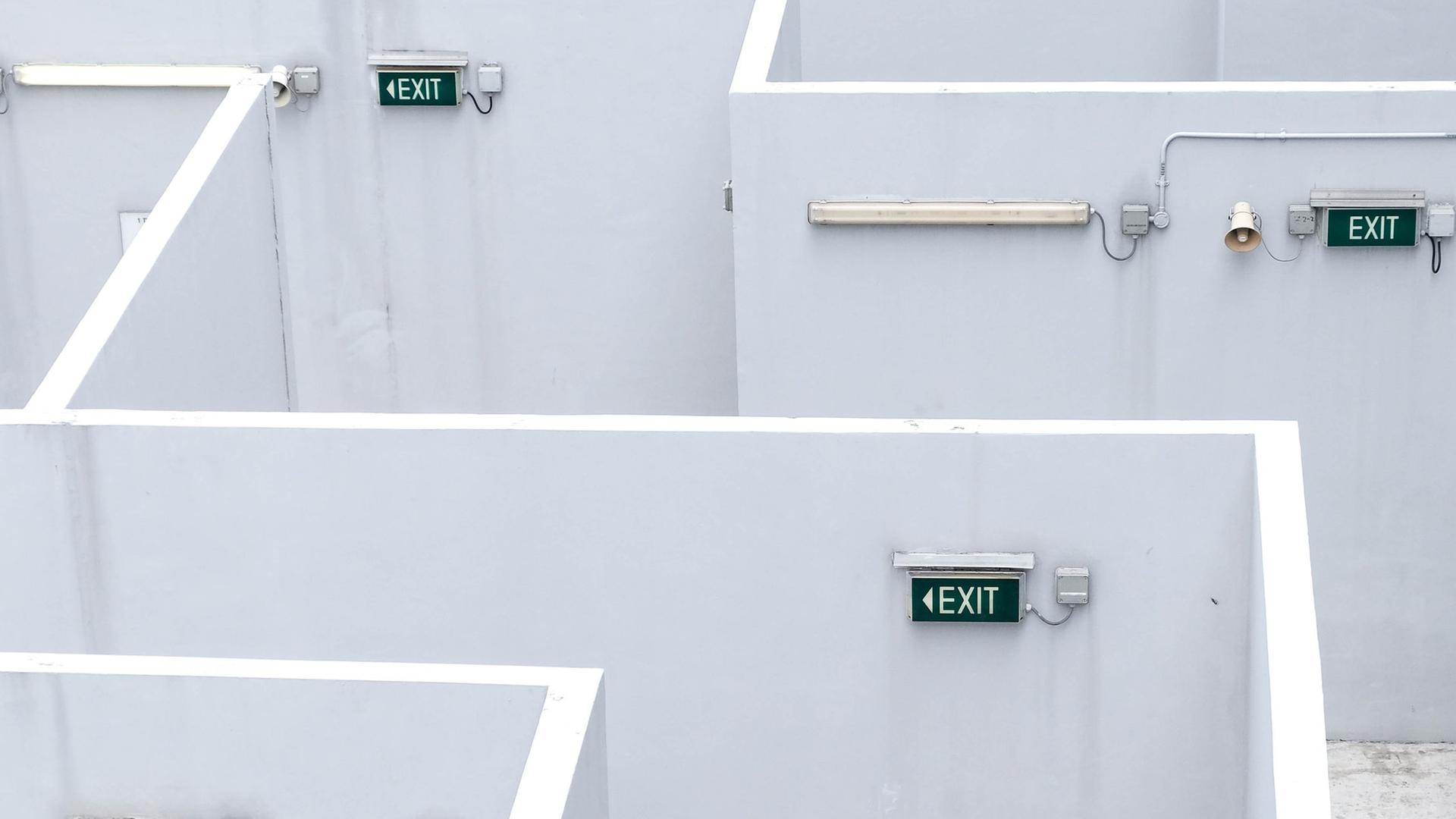 In mehreren labyrinthartigen Gängen hängen "Exit"-Schilder an der Wand. In mehreren labyrinthartigen Gängen hängen "Exit"-Schilder an der Wand.