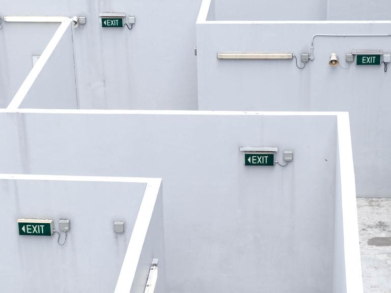 In mehreren labyrinthartigen Gängen hängen "Exit"-Schilder an der Wand.