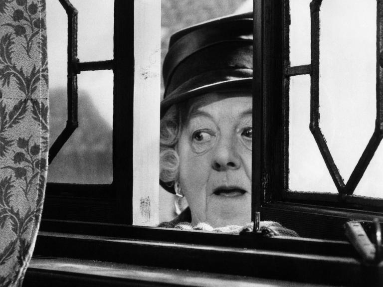 Margaret Rutherford schaut in ihrer Rolle der Miss Marple durch ein leicht geöffnetes Fenster.