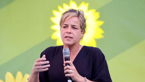 Ein Frau spricht in ein Mikrofon, im Hintergrund sind die Umrisse der gelben Sonnenblume der Grünen zu sehen.