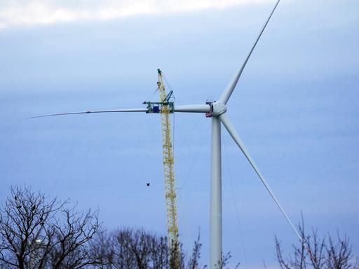 Ein Kran hebt ein Rotorblatt für eine neue Windenergieanlage des deutschen Herstellers Nordex nach oben. Zwei Rotorblätter sind bereits an der Anlage.