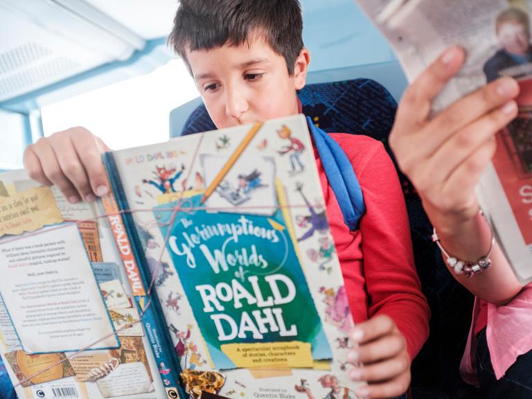 Ein Junge liest in einem öffentlichen Verkehrsmittel ein Buch von Roald Dahl.