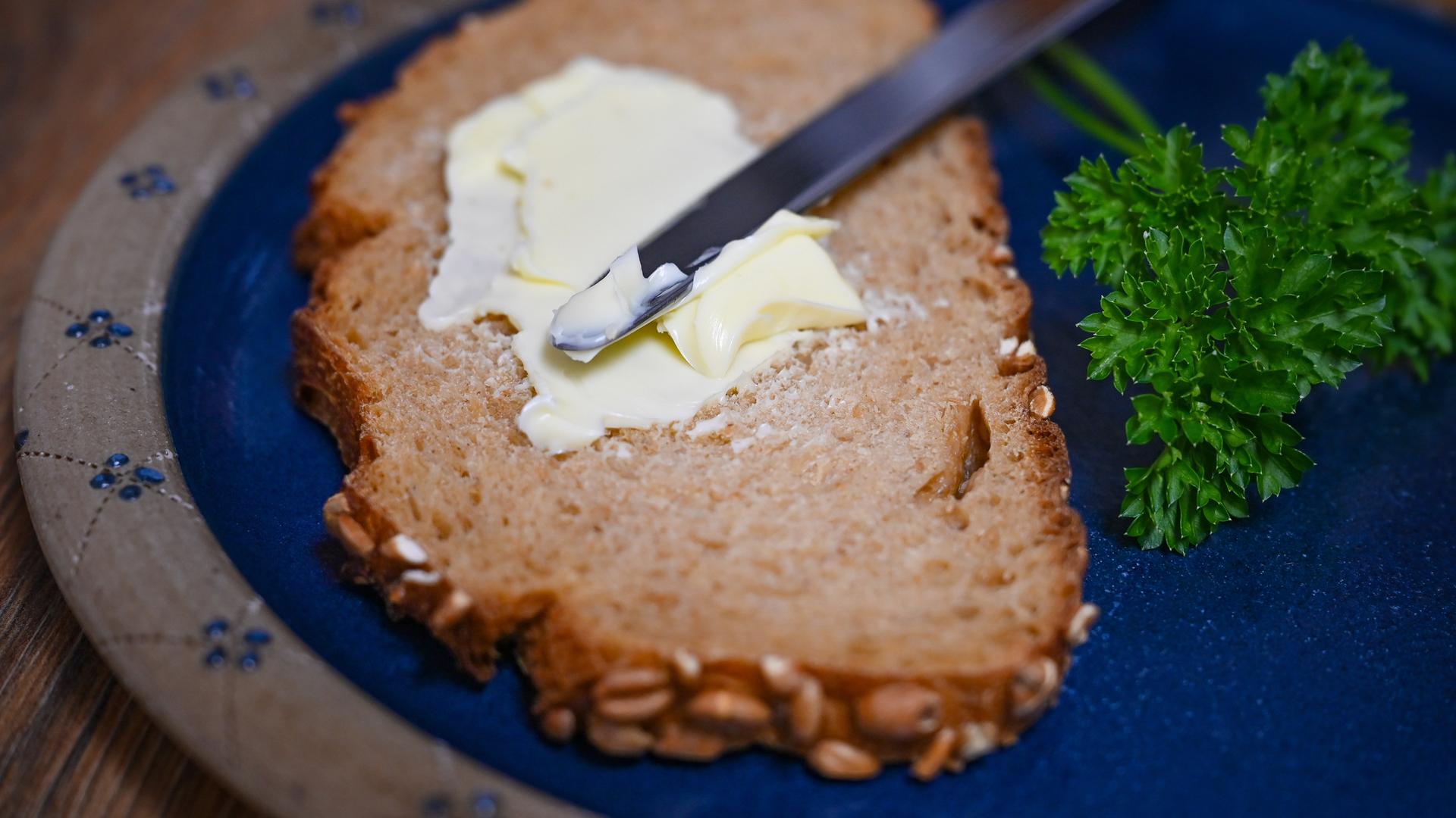 Eine Scheibe Brot liegt zusammen mit einem Messer und Butter auf einem Teller.