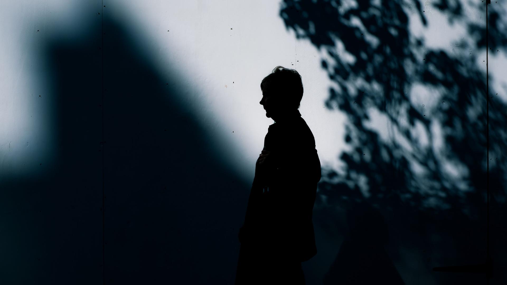 Eine Frau in einemf Parkt steht seitlich vor einem Schatten. Eine Frau in einemf Parkt steht seitlich vor einem Schatten.