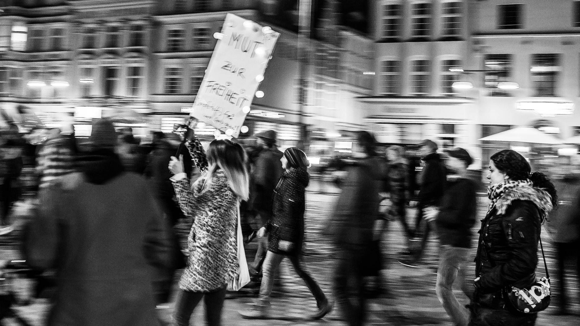 Bewegungsunscharfes Schwarz-Weiß-Foto einer Frau, die auf einer Querdenkerdemo ein Schild mit der Aufschrift "Mut zur Freiheit" trägt. Bewegungsunscharfes Schwarz-Weiß-Foto einer Frau, die auf einer Querdenkerdemo ein Schild mit der Aufschrift "Mut zur Freiheit" trägt.