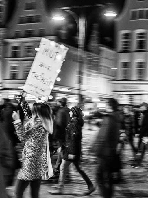 Bewegungsunscharfes Schwarz-Weiß-Foto einer Frau, die auf einer Querdenkerdemo ein Schild mit der Aufschrift "Mut zur Freiheit" trägt.