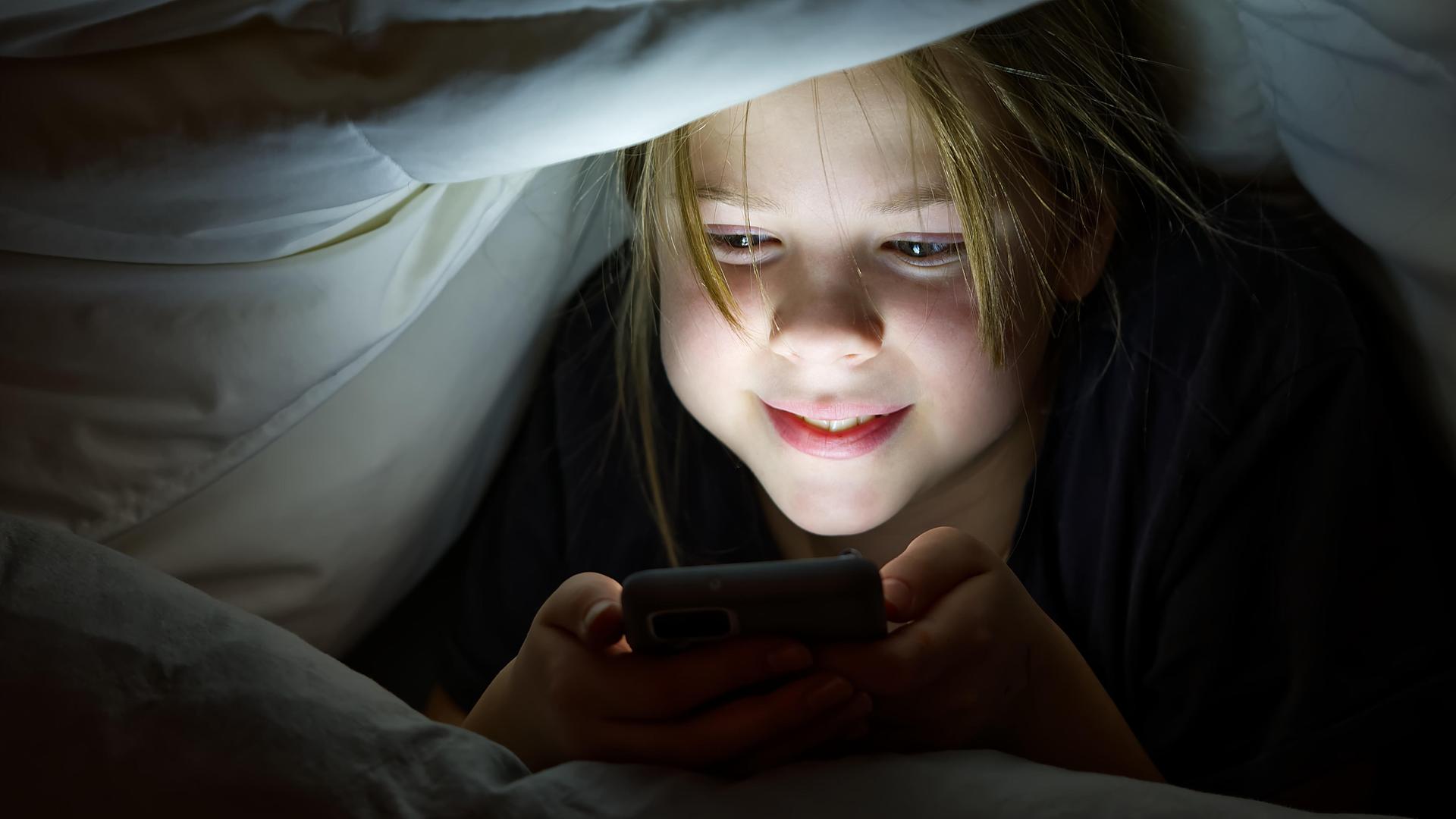 Ein Mädchen liegt auf einem Bett und hat ein Smartphone in der Hand.