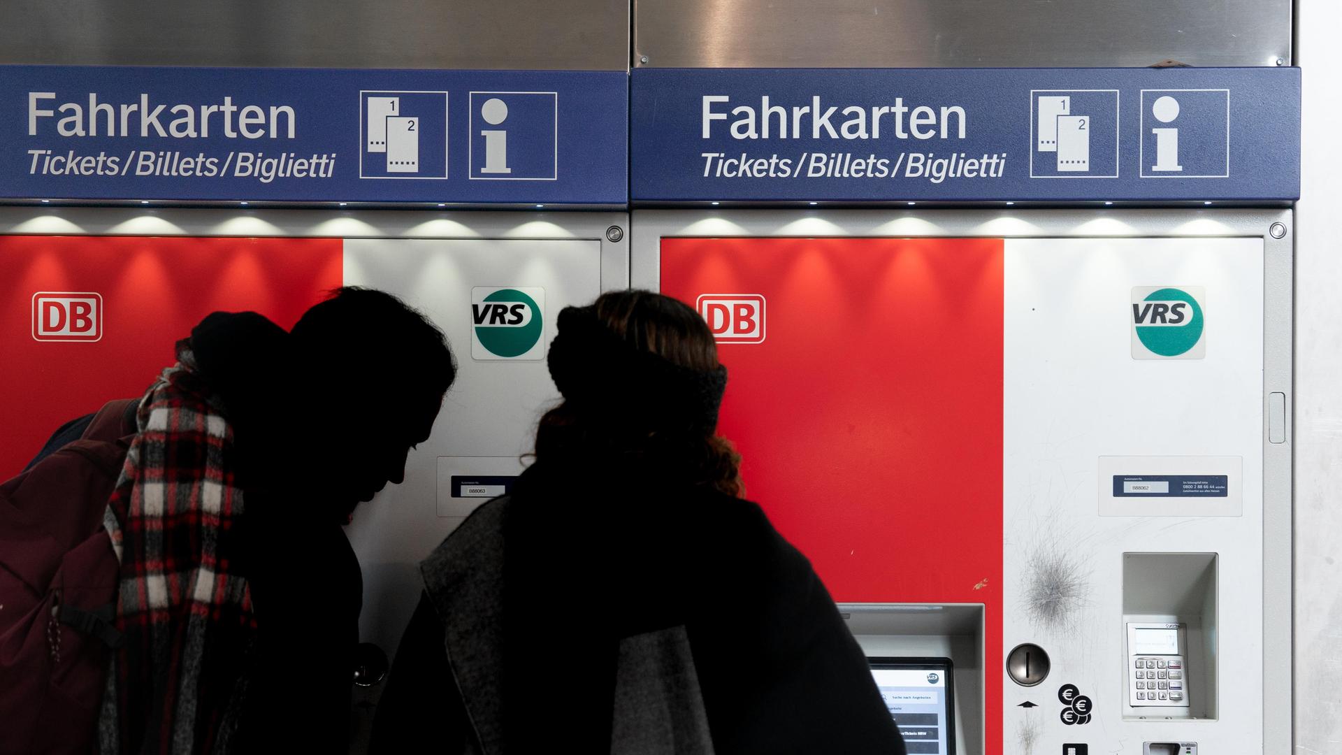 Zwei Personen stehen vor einem Fahrkartenautomat der Deutschen Bahn.