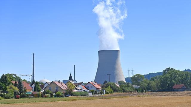 Weißer Dampf steigt aus dem Kühlturm des Atomkraftwerks Isar 2 - im Vordergrund stehen Häuser eines kleinen Dorfes