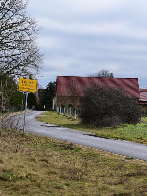 Das Ortseingangsschild des Lychener Ortsteiles Rutenberg: Zu sehen ist eine Landstraße, hinten einige Häuser.