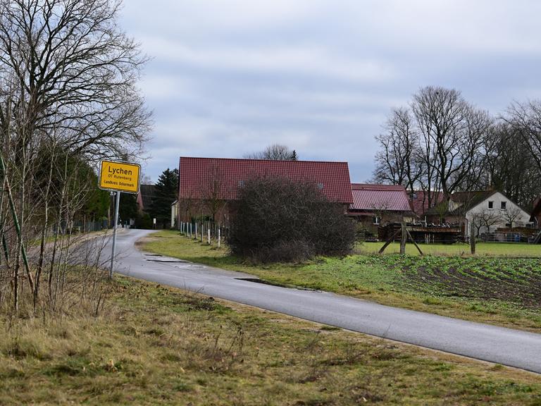 Das Ortseingangsschild des Lychener Ortsteiles Rutenberg: Zu sehen ist eine Landstraße, hinten einige Häuser.