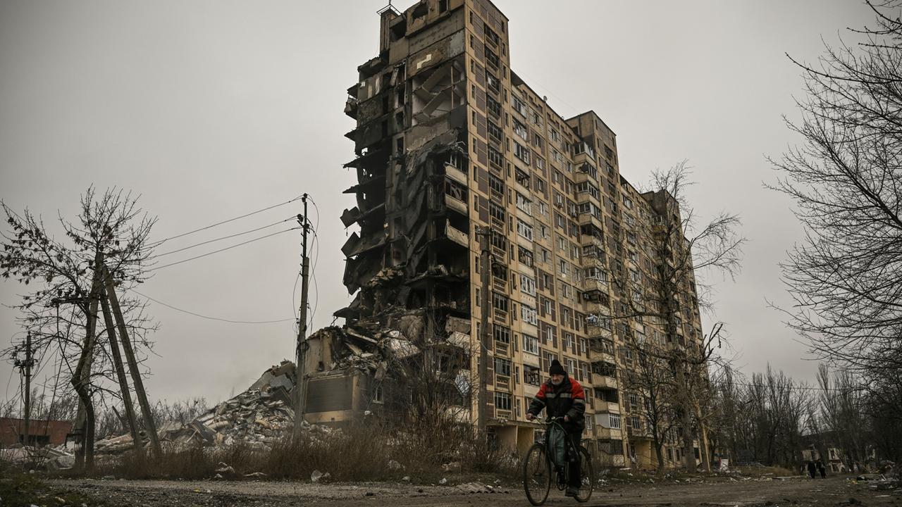Zu sehen ist ein Fahrradfahrer vor einem zerstörten Wohnblock in der Kleinstadt Awdijiwka, Ukraine. 