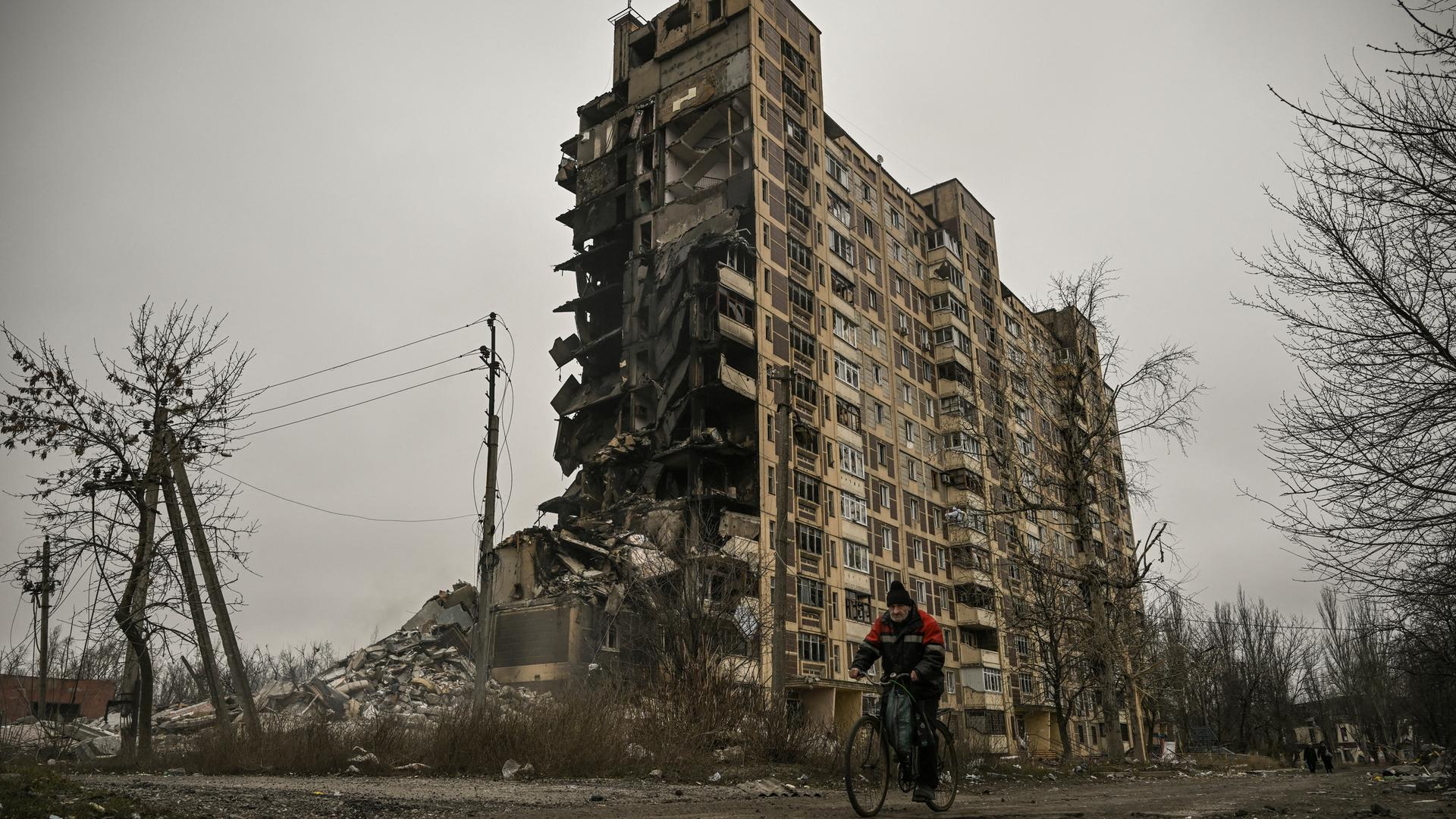 Zu sehen ist ein Fahrradfahrer vor einem zerstörten Wohnblock in der Kleinstadt Awdijiwka, Ukraine.