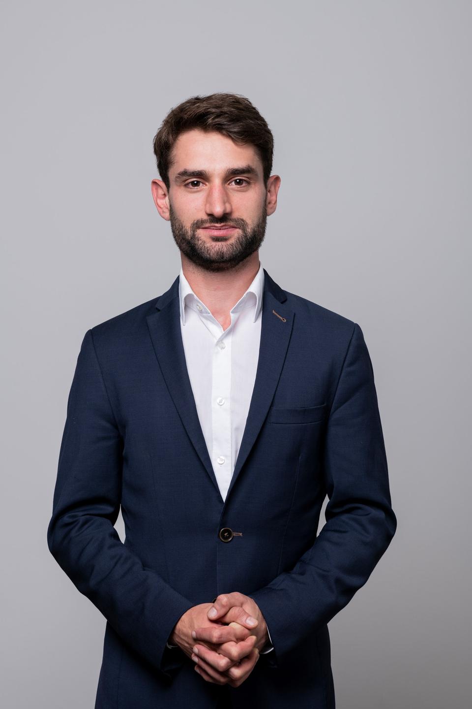 Benjamin Fischer, ein junger Mann mit kurzen dunklen Haaren und kurzem Bart, in weißem Hemd und blauem Sakko, blickt freundlich in die Kamera. Benjamin Fischer, ein junger Mann mit kurzen dunklen Haaren und kurzem Bart, in weißem Hemd und blauem Sakko, blickt freundlich in die Kamera.