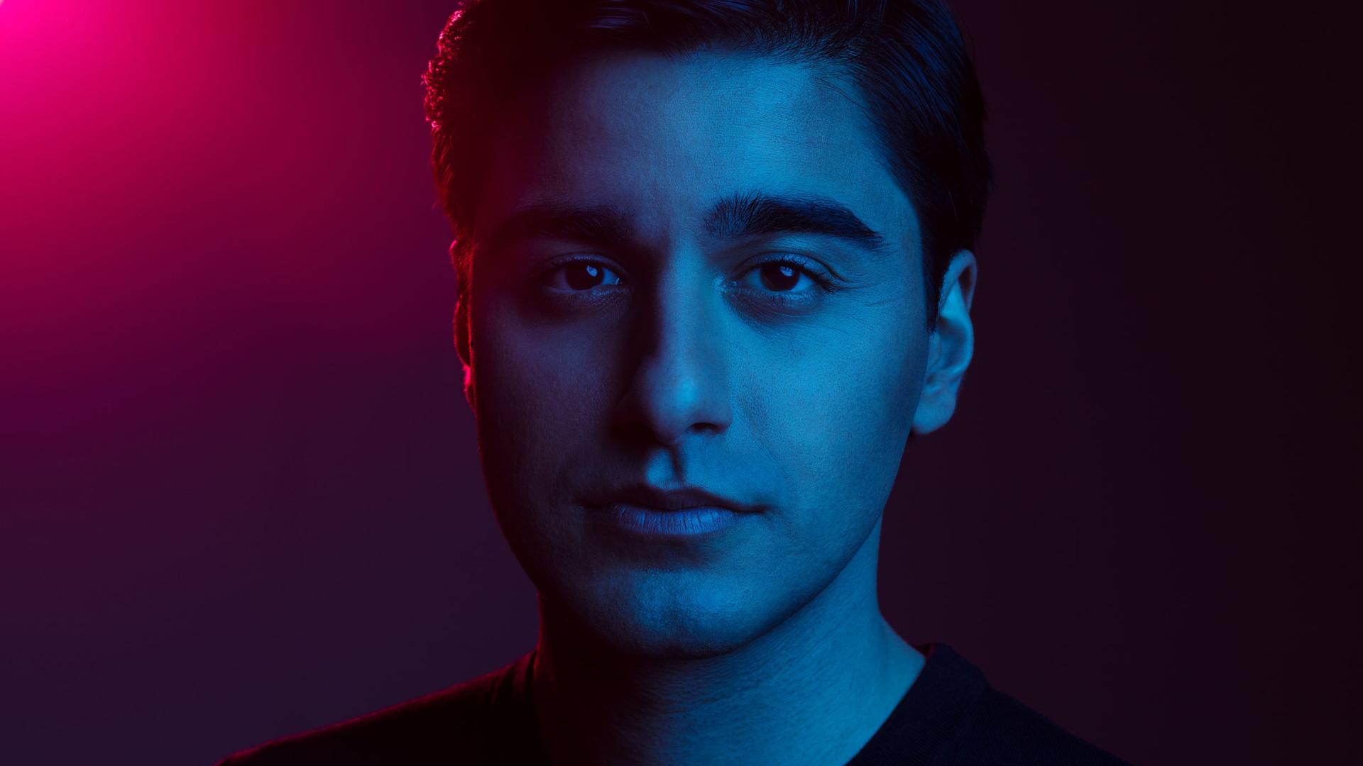 Ein junger Mann mit kurzen, dunklen Haaren steht in blauem Licht, das ins Lila schwenkt. Ein junger Mann mit kurzen, dunklen Haaren steht in blauem Licht, das ins Lila schwenkt.