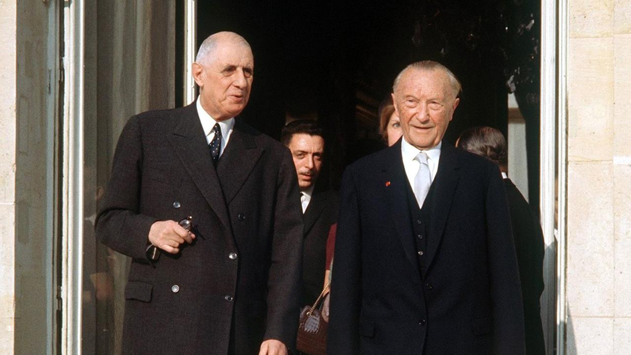 Der französische Staatspräsident Charles de Gaulle und der deutsche Bundeskanzler Konrad Adenauer am 9. Februar 1961, beide in schwarzen Anzügen, vor der offenen Tür des Pariser Elysee Palastes. 