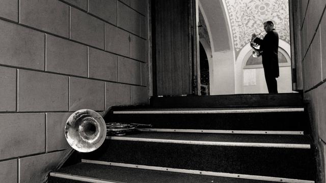 Im Erdgeschoss der Konzerthalle Odessa hat ein Hornist sein Instrument auf einer Treppe abgelegt. Ein weiterer spielt in der großen Halle, die sich am Ende der Treppe eröffnet.