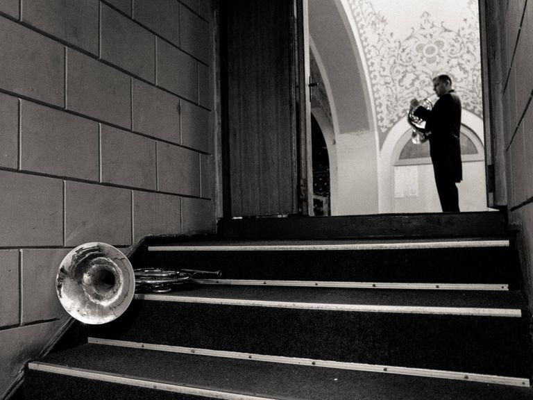 Im Erdgeschoss der Konzerthalle Odessa hat ein Hornist sein Instrument auf einer Treppe abgelegt. Ein weiterer spielt in der großen Halle, die sich am Ende der Treppe eröffnet.