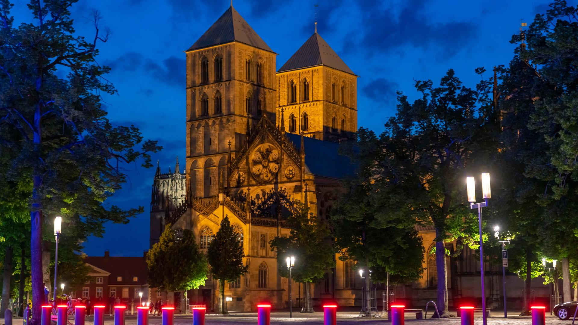 Sankt-Paulus-Dom in der Altstadt Münster in der Dämmerung mit roten Warnlichtern an Pollern davor. Sankt-Paulus-Dom in der Altstadt Münster in der Dämmerung mit roten Warnlichtern an Pollern davor.