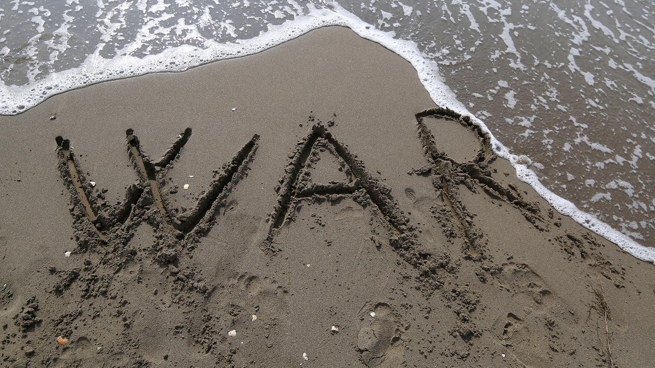 Die Buchstaben "W A R" sind in den Sand an einem Strand geschrieben.