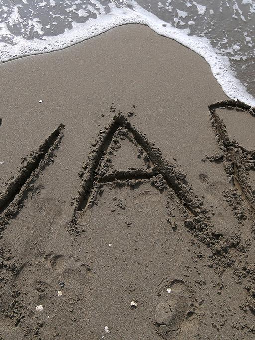 Die Buchstaben "W A R" sind in den Sand an einem Strand geschrieben.
