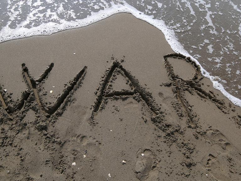 Die Buchstaben "W A R" sind in den Sand an einem Strand geschrieben.