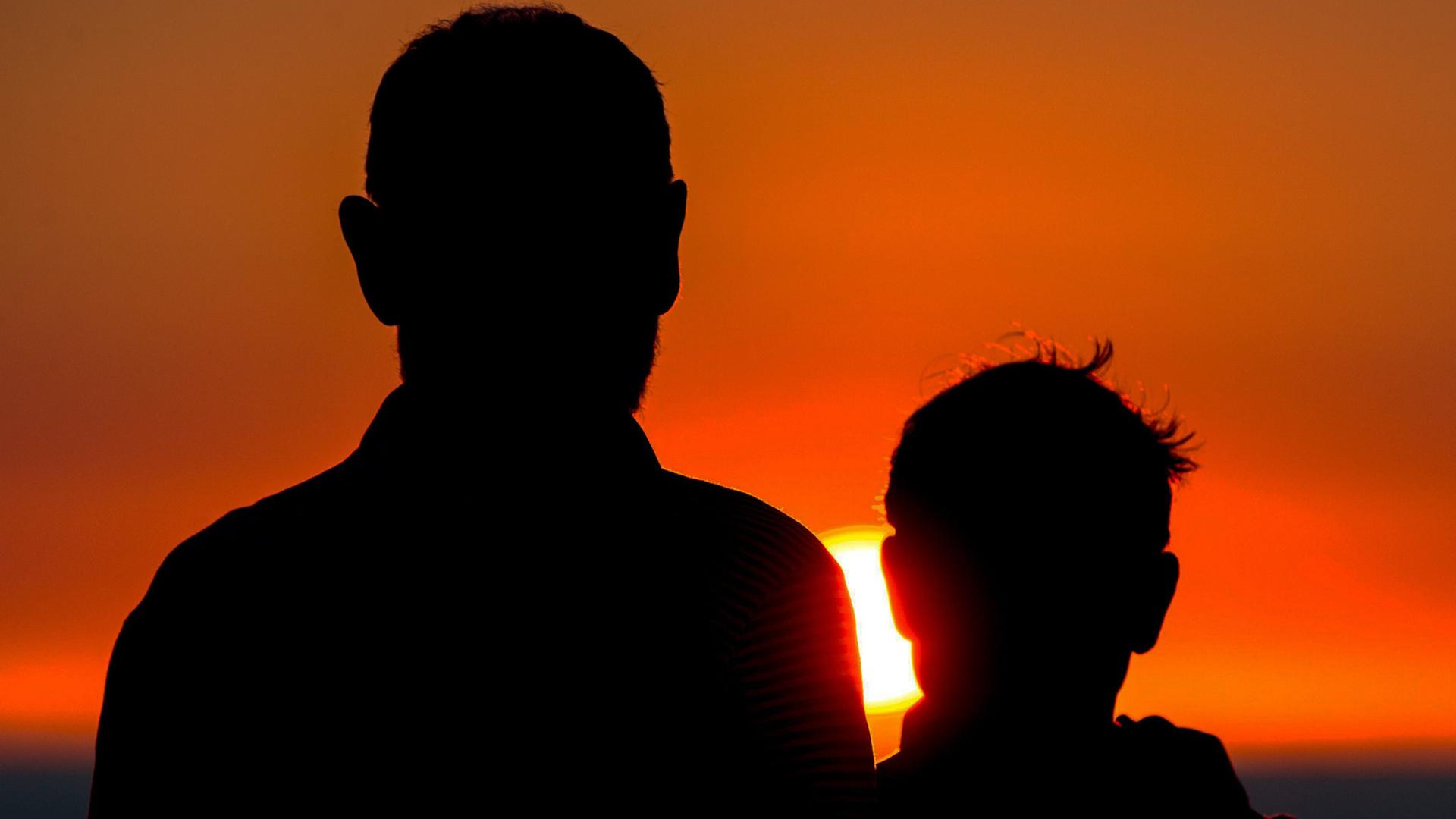 Vater und Sohn stehen mit dem Rücken zur Kamera und betrachten den Sonnenuntergang. Vater und Sohn stehen mit dem Rücken zur Kamera und betrachten den Sonnenuntergang.