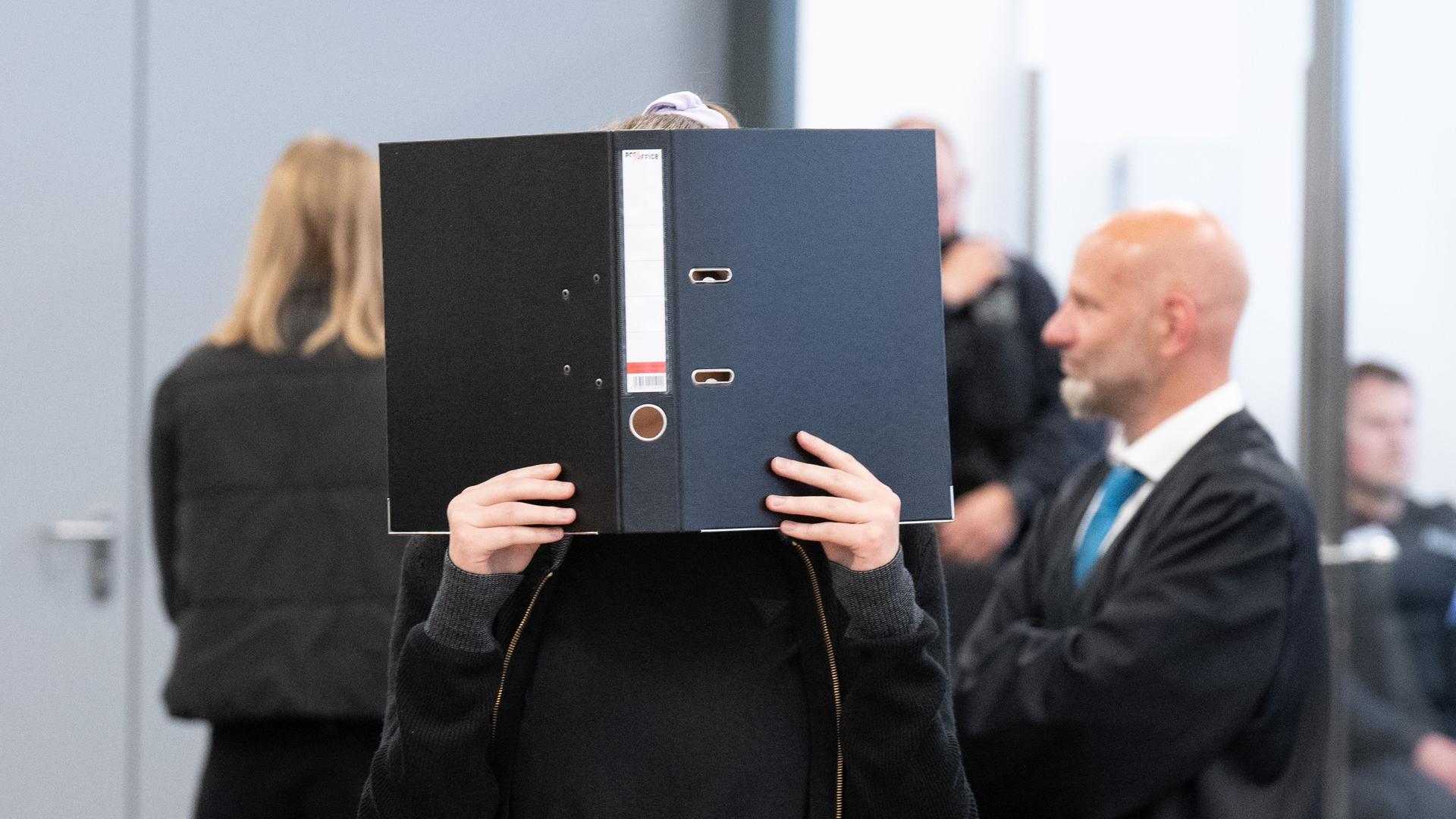 Die Angeklagte Lina E. steht bei der Fortsetzung des Prozesses im Oberlandesgericht (OLG) Dresden im Verhandlungssaal und hält einen Aktenordner vor ihr Gesicht. Das Oberlandesgericht hat die mutmaßliche Linksextremistin Lina E. zu fünf Jahren und drei Monaten Freiheitsstrafe verurteilt. Nach Auffassung des Gerichts gehörte sie einer Gruppe an, die Überfälle auf Mitglieder der rechten Szene begangen hat.