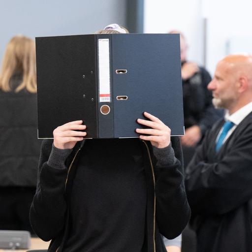 Die Angeklagte Lina E. steht bei der Fortsetzung des Prozesses im Oberlandesgericht (OLG) Dresden im Verhandlungssaal und hält einen Aktenordner vor ihr Gesicht.