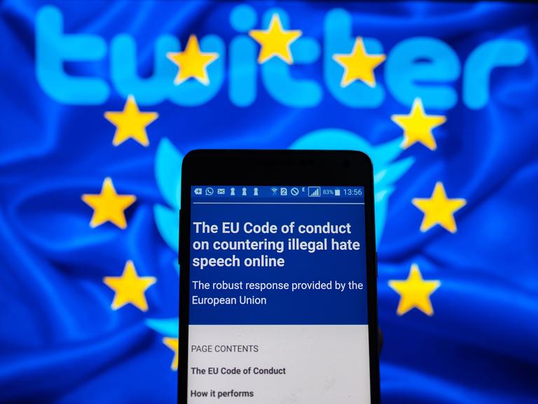 Auf einem Handy-Display erscheint der EU-Verhaltenskodex zur Bekämpfung von Hasskommentaren und im Hintergrund ein Twitter-Logo.