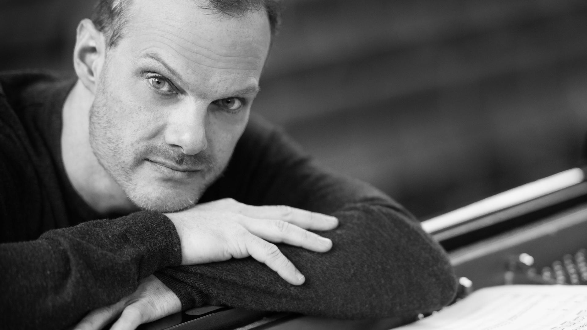 Der Pianist Lars Vogt sitzt am Klavier und hat die Arme auf das Instrument gestützt und schaut in die Kamera, während vor ihm ein aufgeschlagenes Notenheft liegt. Der Pianist Lars Vogt sitzt am Klavier und hat die Arme auf das Instrument gestützt und schaut in die Kamera, während vor ihm ein aufgeschlagenes Notenheft liegt.