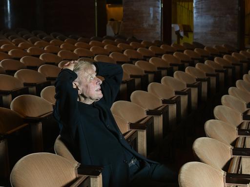Der Theaterregisseur Claus Peymann sitzt im Zuschauerraum zwischen lauter leeren Stuhlreihen. 