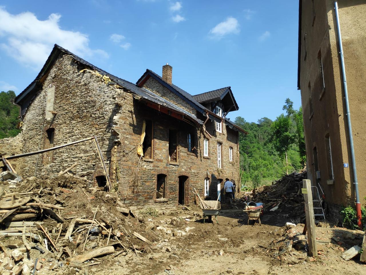 Vor einem alten Backsteinhaus liegen Schutt und Trümmer, eine Menschen und Schubkarren stehen davor. Vor einem alten Backsteinhaus liegen Schutt und Trümmer, eine Menschen und Schubkarren stehen davor.