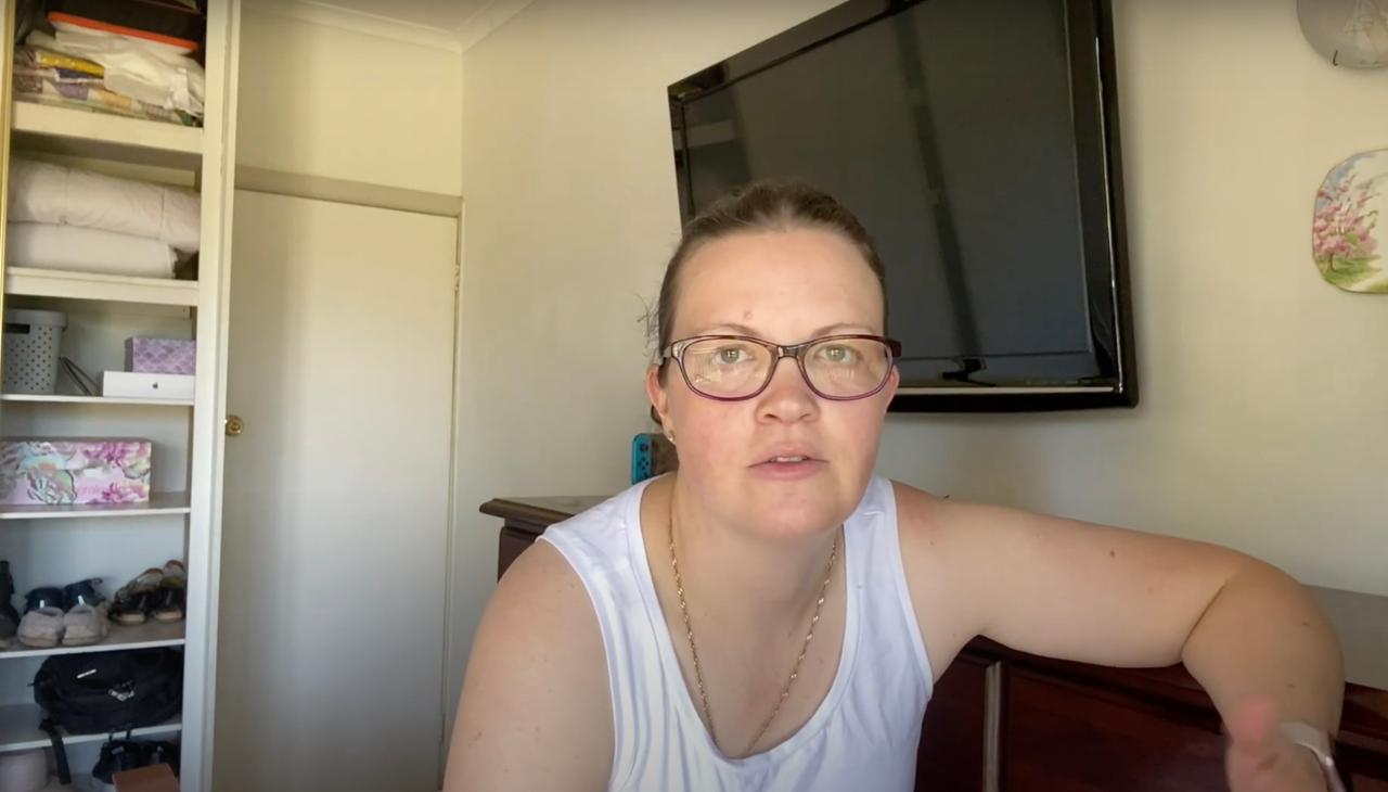Eine junge Frau in ärmellosem weißen Shirt sitzt in einer Wohnung vor einem riesigen Fernsehbildschirm. Eine junge Frau in ärmellosem weißen Shirt sitzt in einer Wohnung vor einem riesigen Fernsehbildschirm.