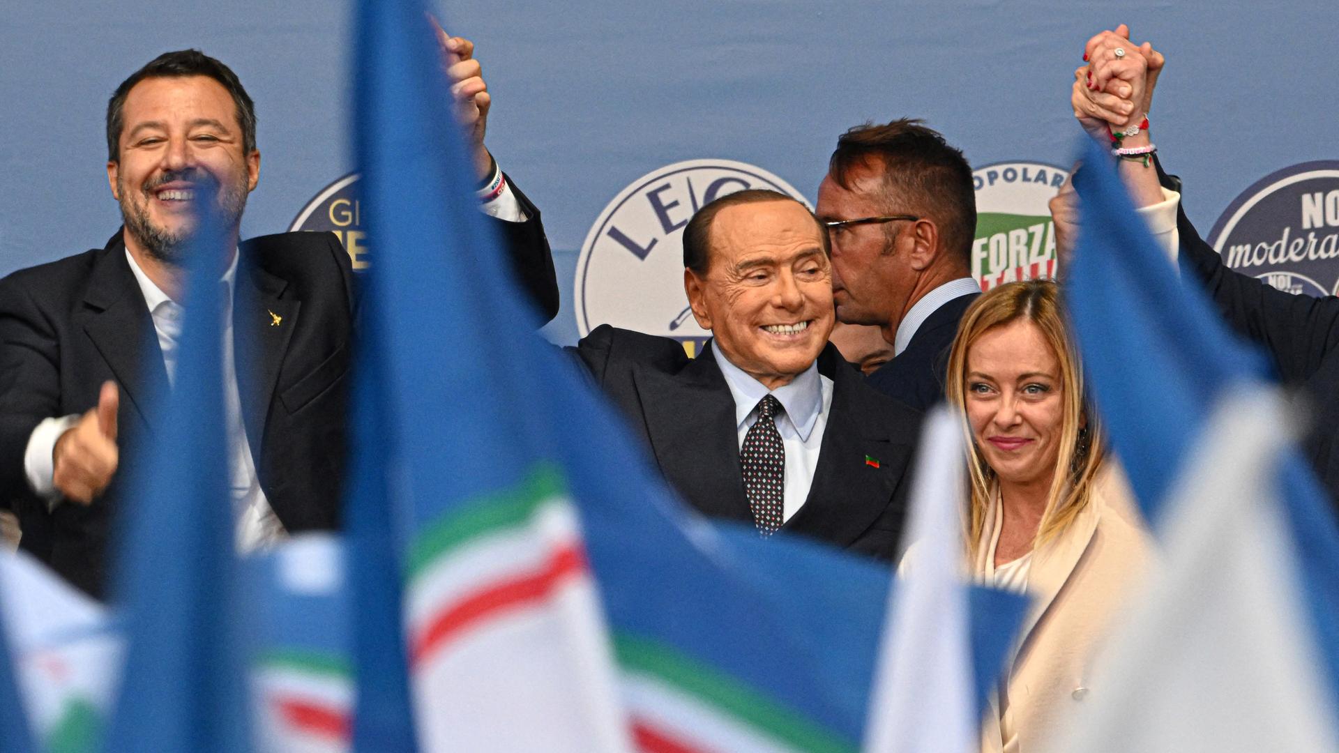 Von links: Chef der Lega Partei Matteo Salvini, Forza Chef Silvio Berlusconi und Giorgia Meloni zusammen auf einer Wahlbühne am 22. September in Rom, Italien. Vor ihnen wehen Fahnen.