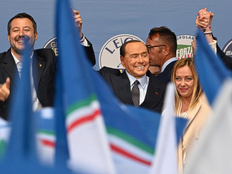 Von links: Chef der Lega Partei Matteo Salvini, Forza Chef Silvio Berlusconi und Giorgia Meloni zusammen auf einer Wahlbühne am 22. September in Rom, Italien. Vor ihnen wehen Fahnen.